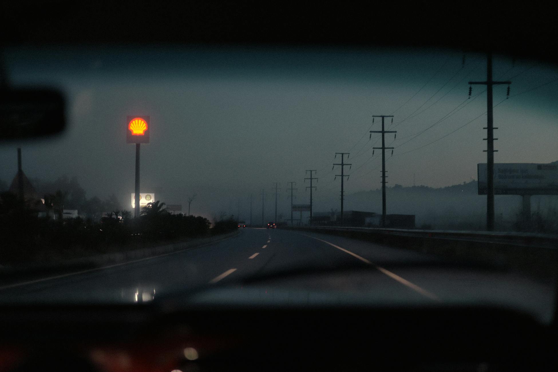 View from a car window of a misty highway at dusk featuring a glowing Shell sign.