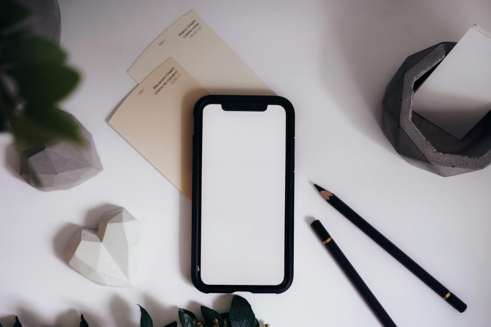 Flat lay of modern desktop with smartphone mockup, pencils, and decor against a clean background.